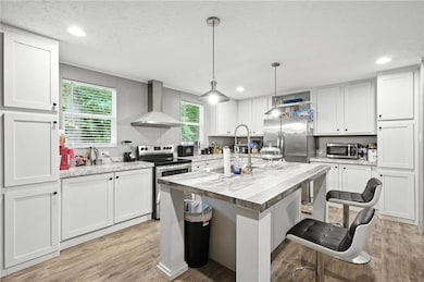 Kitchen featuring stainless steel appliances, wall chimney exhaust hood, light wood-style floors, white cabinetry, and recessed lighting