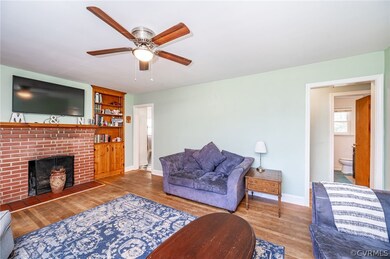 Living room with a brick fireplace, built in shelves, ceiling fan, and dark hardwood / wood-style flooring