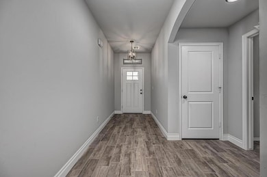 Doorway with arched walkways, wood finished floors, a chandelier, and baseboards