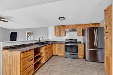 This kitchen features rustic wooden cabinetry, modern stainless steel appliances, and a sleek black countertop. The open layout and light wood flooring create a spacious and inviting atmosphere.