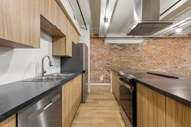 Kitchen featuring range with electric cooktop, brick wall, island range hood, sink, and stainless steel dishwasher