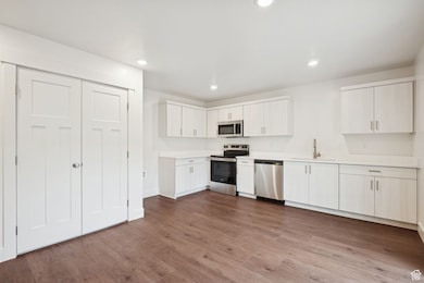 Kitchen with stainless steel appliances, light countertops, recessed lighting, dark wood-type flooring, and white cabinetry