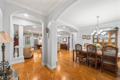 Dining area with light wood-type flooring, arched walkways, crown molding, ornate columns, and a chandelier