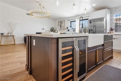 Kitchen with beverage cooler, stainless steel refrigerator with ice dispenser, dark brown cabinetry, white cabinetry, and pendant lighting