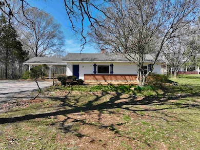 Single story home featuring driveway, a front yard, a chimney, brick siding, and a carport
