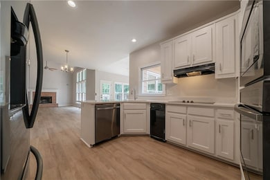 Kitchen with freestanding refrigerator, dishwasher, under cabinet range hood, built in microwave, and white cabinetry