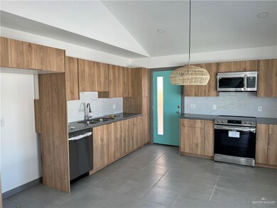 Kitchen with stainless steel appliances, a sink, backsplash, modern cabinets, and brown cabinetry