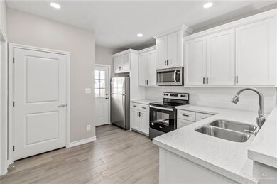 Kitchen with tasteful backsplash, light wood-type flooring, sink, white cabinets, and appliances with stainless steel finishes