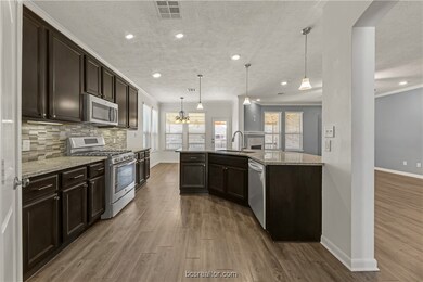 Kitchen featuring sink, light stone counters, decorative light fixtures, stainless steel appliances, and decorative backsplash