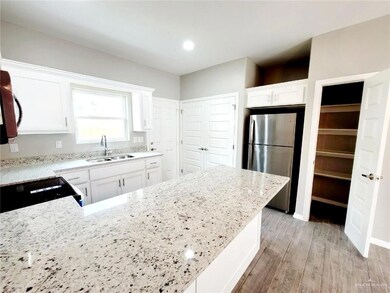 Kitchen with black range, a sink, light wood-type flooring, light stone countertops, and freestanding refrigerator