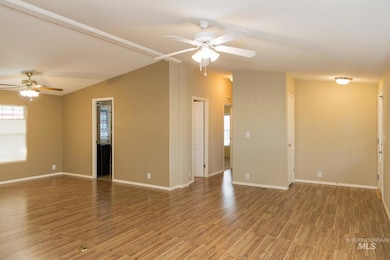 Empty room with ceiling fan, light wood-style flooring, and vaulted ceiling