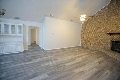 Unfurnished living room with lofted ceiling, brick wall, light wood-type flooring, a brick fireplace, and ceiling fan