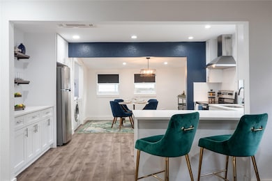 Kitchen with wall chimney exhaust hood, appliances with stainless steel finishes, a breakfast bar area, white cabinets, and light wood finished floors