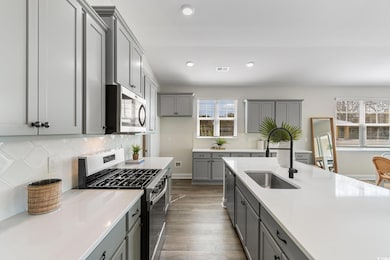 Kitchen with appliances with stainless steel finishes, a sink, gray cabinets, dark wood-style flooring, and light countertops