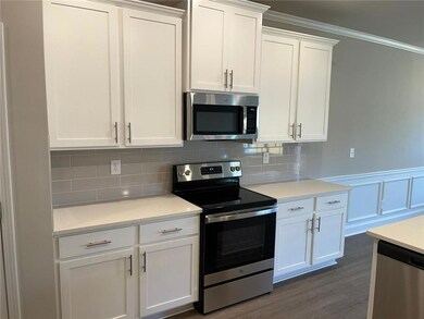 Kitchen featuring appliances with stainless steel finishes, white cabinets, backsplash, quartz countertops, and crown molding.
