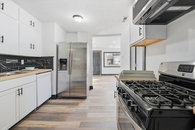 Kitchen with stainless steel appliances, ventilation hood, white cabinetry, decorative backsplash, and light wood-type flooring
