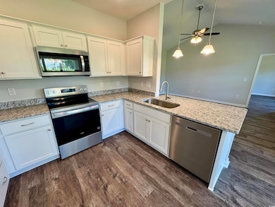 Kitchen featuring appliances with stainless steel finishes, white cabinetry, a peninsula, dark wood-style floors, and lofted ceiling