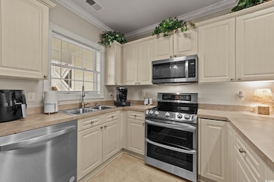 Kitchen featuring appliances with stainless steel finishes, a sink, light tile patterned floors, light countertops, and ornamental molding