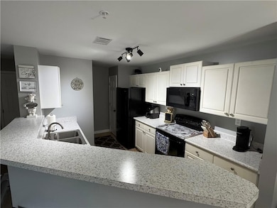 Kitchen with black appliances, a sink, light countertops, white cabinetry, and baseboards