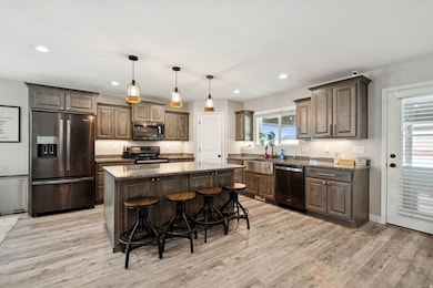 Kitchen with appliances with stainless steel finishes, hanging light fixtures, dark stone counters, dark brown cabinets, and light wood finished floors