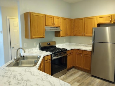 Kitchen with appliances with stainless steel finishes, light countertops, light wood-type flooring, under cabinet range hood, and brown cabinets