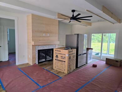 Living room with a tiled fireplace, ceiling fan, beamed ceiling, and wood finished floors