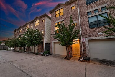 This photo shows a row of modern, three-story brick townhouses with attached garage. The setting is serene, featuring well-maintained trees and a beautiful sunset sky.