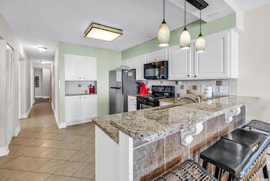 Kitchen with backsplash, black appliances, white cabinetry, a breakfast bar area, and a peninsula