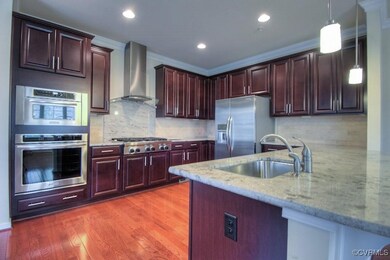 Kitchen with wall chimney range hood, stainless steel appliances, a sink, ornamental molding, and decorative light fixtures