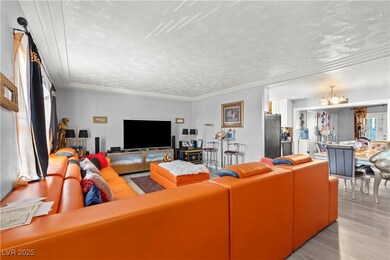 Living room featuring a textured ceiling, light wood-style flooring, crown molding, and a chandelier
