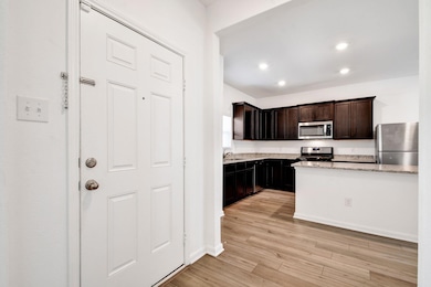 Kitchen featuring stainless steel appliances, light stone counters, light wood-style flooring, recessed lighting, and dark brown cabinets