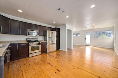 Kitchen with stainless steel appliances, dark brown cabinets, light wood finished floors, recessed lighting, and open floor plan