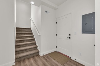 Entryway featuring electric panel, wood finished floors, baseboards, and stairway