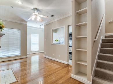 Unfurnished living room with built in shelves, crown molding, light wood-type flooring, a ceiling fan, and stairs
