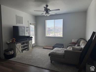 Living room with a textured ceiling, wood finished floors, and a ceiling fan