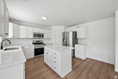 Kitchen with appliances with stainless steel finishes, a center island, white cabinets, light wood-style floors, and light stone counters