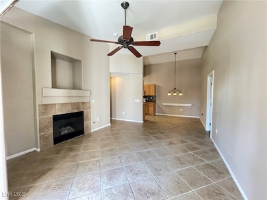 Unfurnished living room featuring light tile patterned flooring, ceiling fan, a tiled fireplace, a chandelier, and a high ceiling