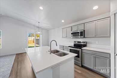 Kitchen with gray cabinets, stainless steel appliances, lofted ceiling, a kitchen island with sink, and decorative light fixtures