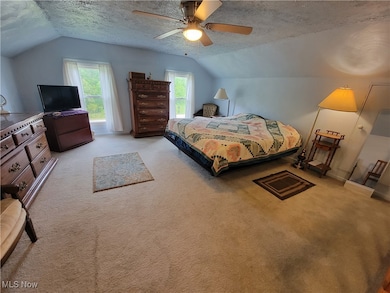 Carpeted bedroom featuring a textured ceiling, lofted ceiling, and ceiling fan