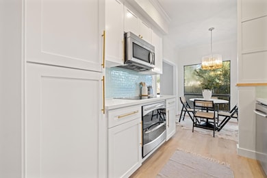 Kitchen with decorative backsplash, light wood-style floors, white cabinetry, and hanging light fixtures