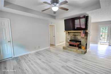 Unfurnished living room featuring a ceiling fan, a stone fireplace, wood finished floors, a raised ceiling, and baseboards