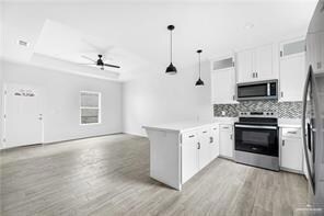 Kitchen featuring ceiling fan, open floor plan, a tray ceiling, appliances with stainless steel finishes, and a peninsula