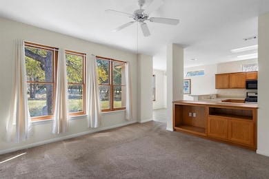 Kitchen featuring brown cabinetry, light colored carpet, plenty of natural light, and a ceiling fan
