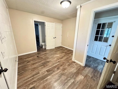 Unfurnished bedroom with a textured ceiling, dark wood-type flooring, and a closet