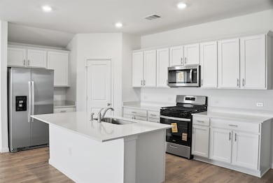 Kitchen with stainless steel appliances, white cabinets, dark wood-style flooring, an island with sink, and recessed lighting