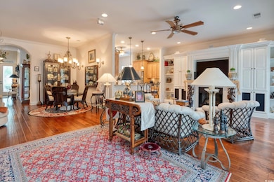 Living room featuring ceiling fan, arched walkways, a chandelier, ornamental molding, and hardwood / wood-style flooring