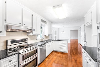 Kitchen featuring stainless steel appliances, a peninsula, dark stone countertops, a textured ceiling, and a chandelier