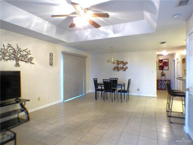 Dining room with light tile patterned floors, a raised ceiling, ceiling fan with notable chandelier, and visible vents