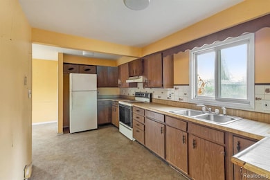 Kitchen featuring white appliances, light countertops, tasteful backsplash, under cabinet range hood, and brown cabinets