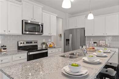 Kitchen featuring stainless steel appliances, a sink, white cabinets, decorative light fixtures, and a kitchen breakfast bar
